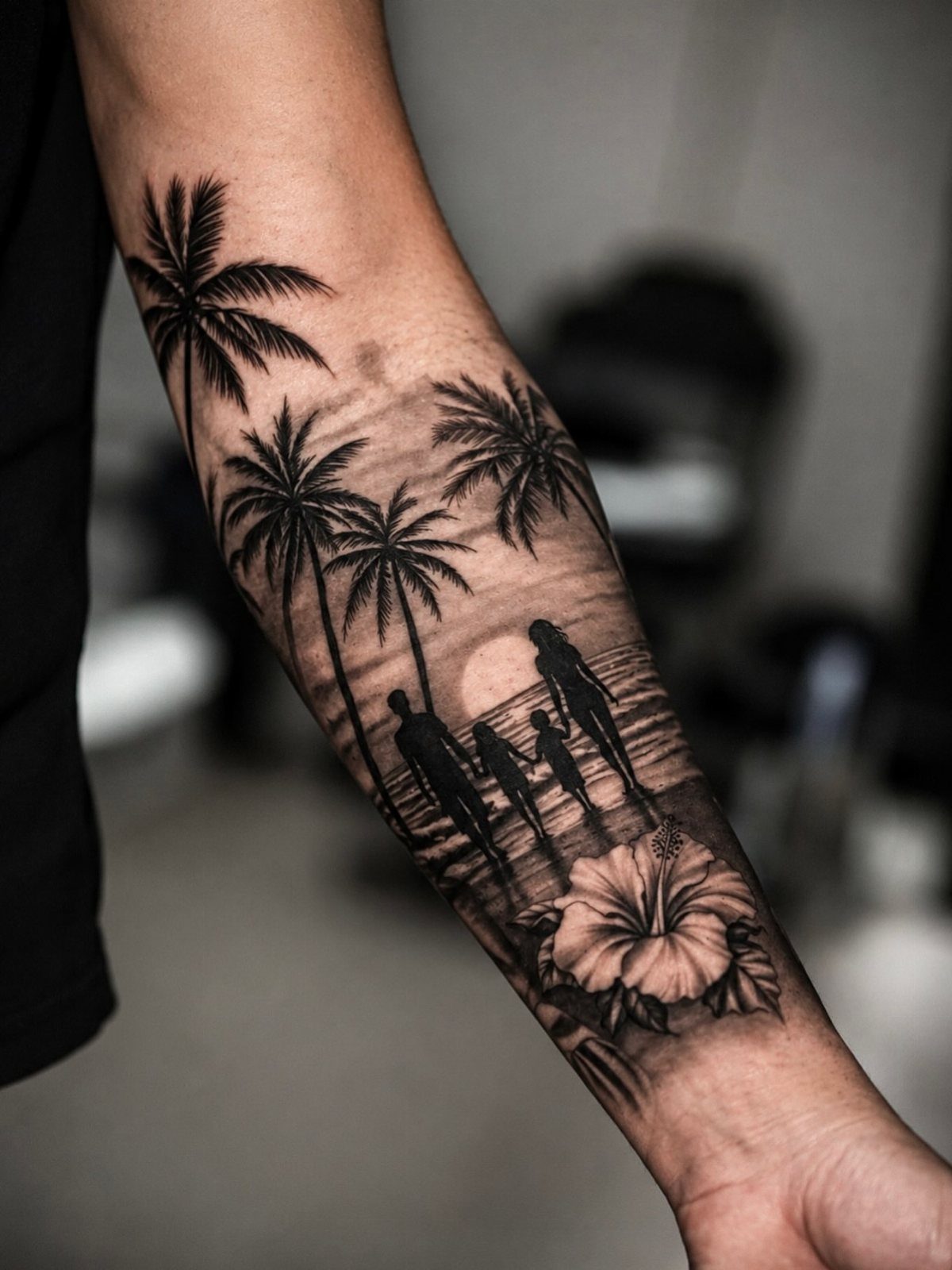 A black and grey forearm tattoo featuring palm trees, a sunset, and silhouettes walking on a beach.