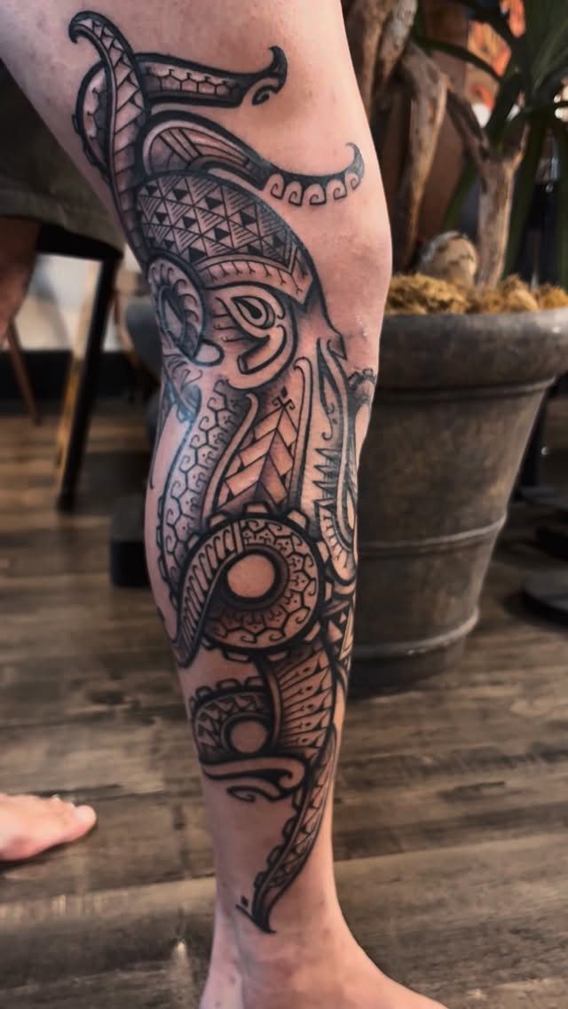 A large black ink tribal tattoo with geometric patterns covering a person's lower leg.