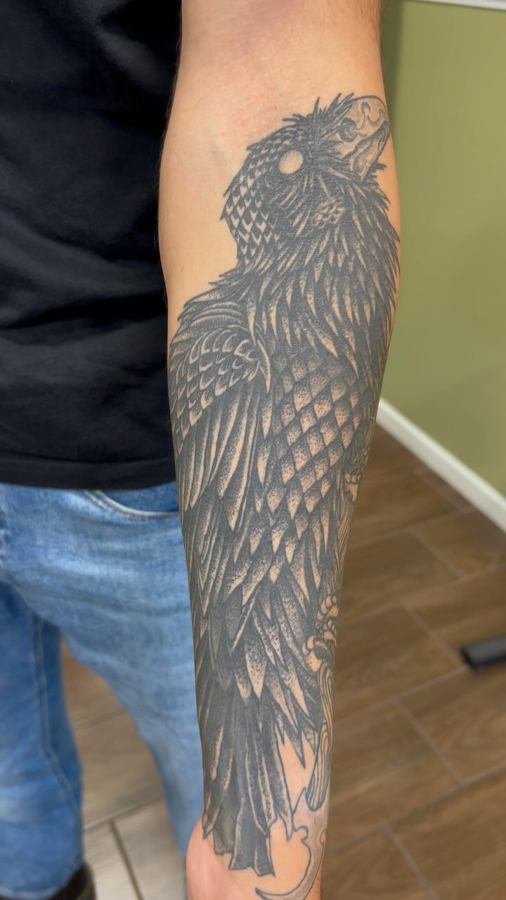 10 Traditional Cover Up Tattoo Ideas for Old Ink 4 A large black ink bird tattoo with detailed feather patterns on a person's forearm.