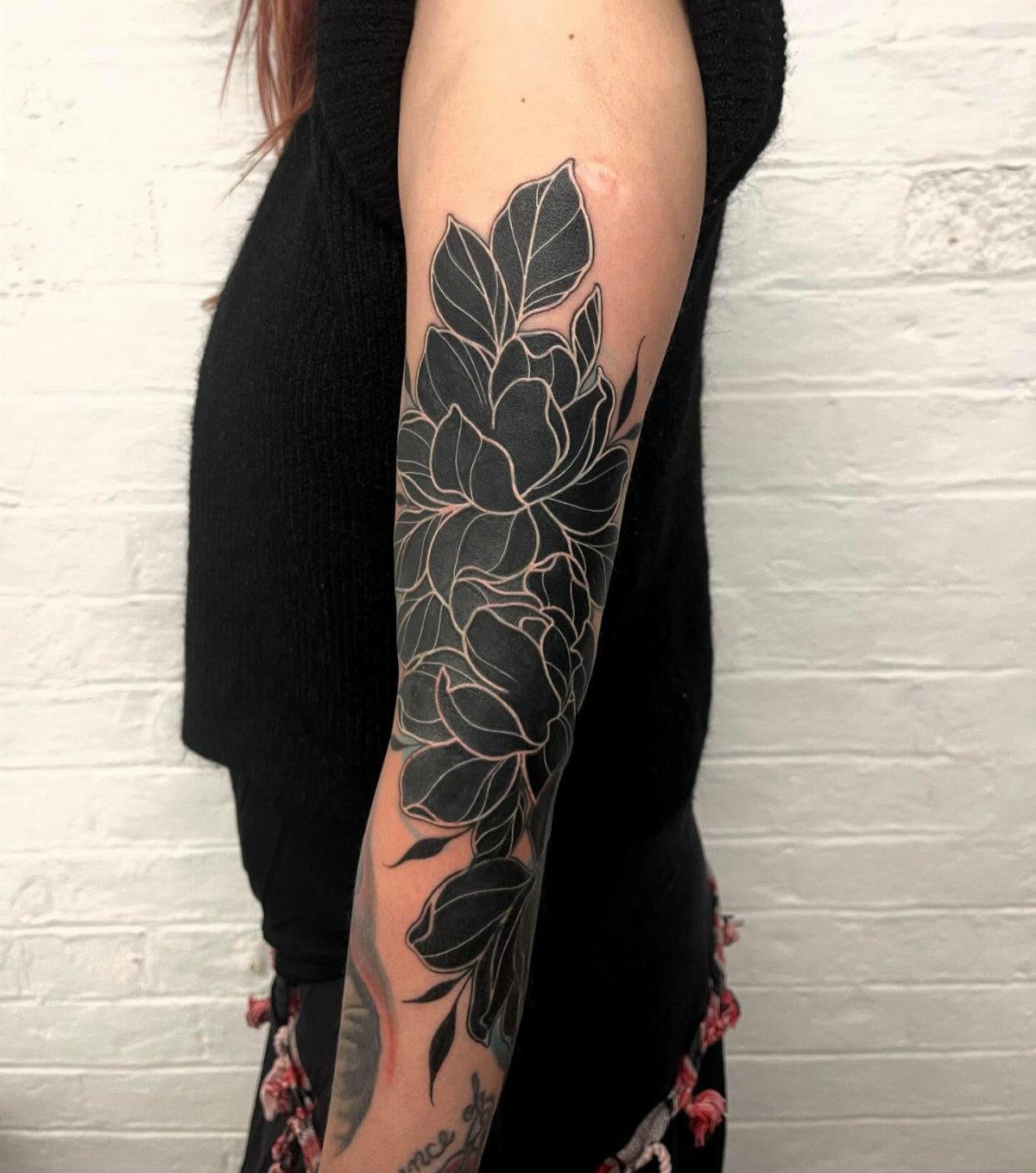 10 Traditional Cover Up Tattoo Ideas for Old Ink 1 Large black and grey floral tattoo covering a person's arm against a white brick wall.