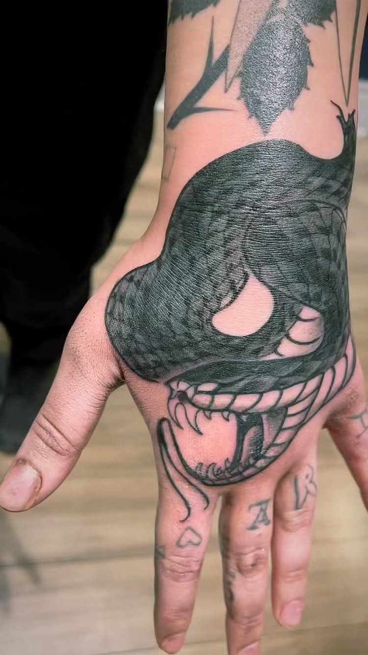 10 Traditional Cover Up Tattoo Ideas for Old Ink 2 A large black ink snake tattoo covering the back of a person's hand and wrist.