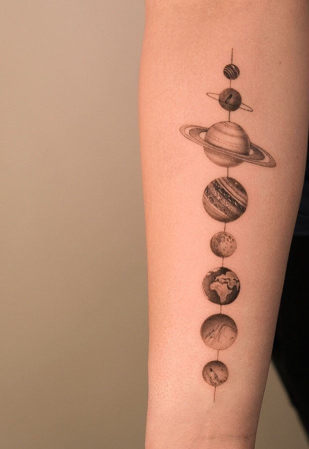 Universe Tattoo Pattern: 8 Space-Inspired Designs for Your Next Ink 1 A vertical tattoo of various planets and Saturn on a person's forearm.