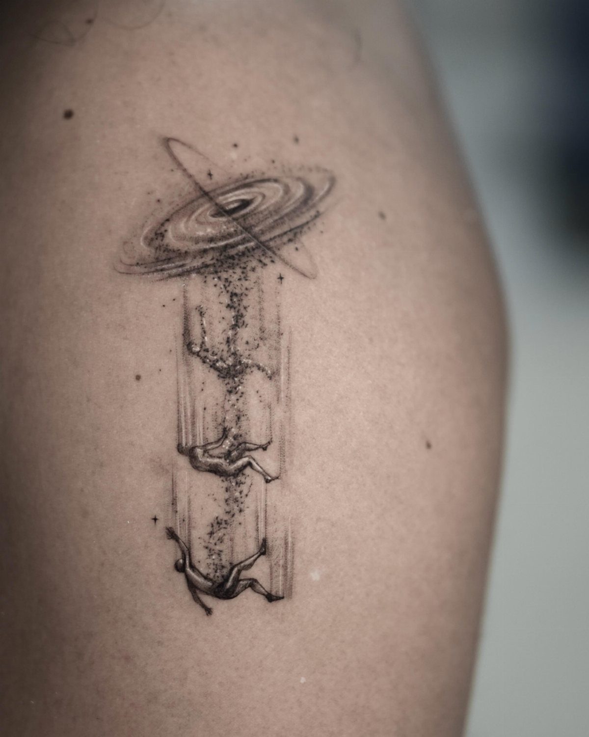 Universe Tattoo Pattern: 8 Space-Inspired Designs for Your Next Ink 7 Black ink tattoo on skin showing a swirling galaxy with orbital rings and falling human figures.