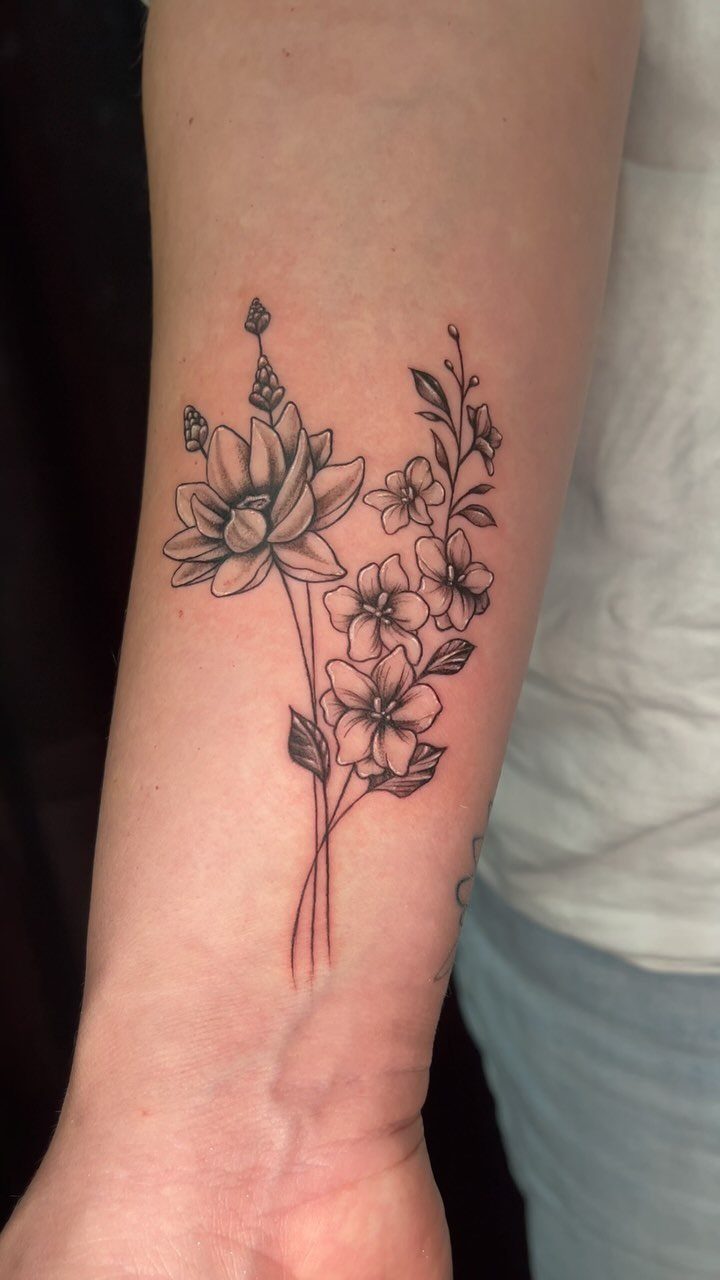 Black ink floral tattoo with layered petals and small blossoms on a person's forearm.