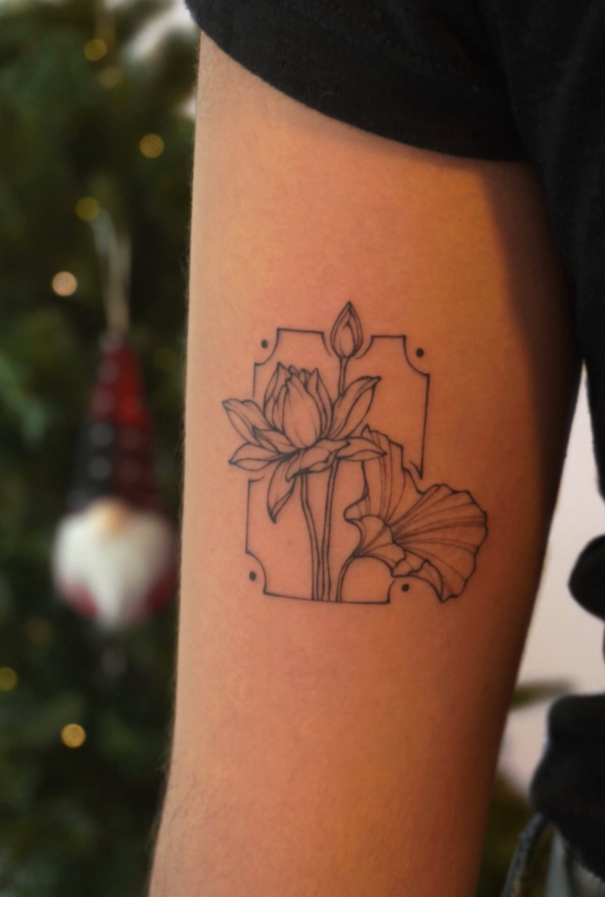 Black ink water lily tattoo with geometric lines on a person's arm.