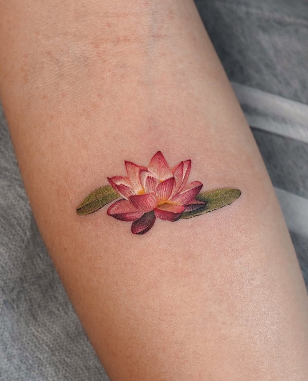 A colorful pink and yellow water lily tattoo with green leaves on skin.