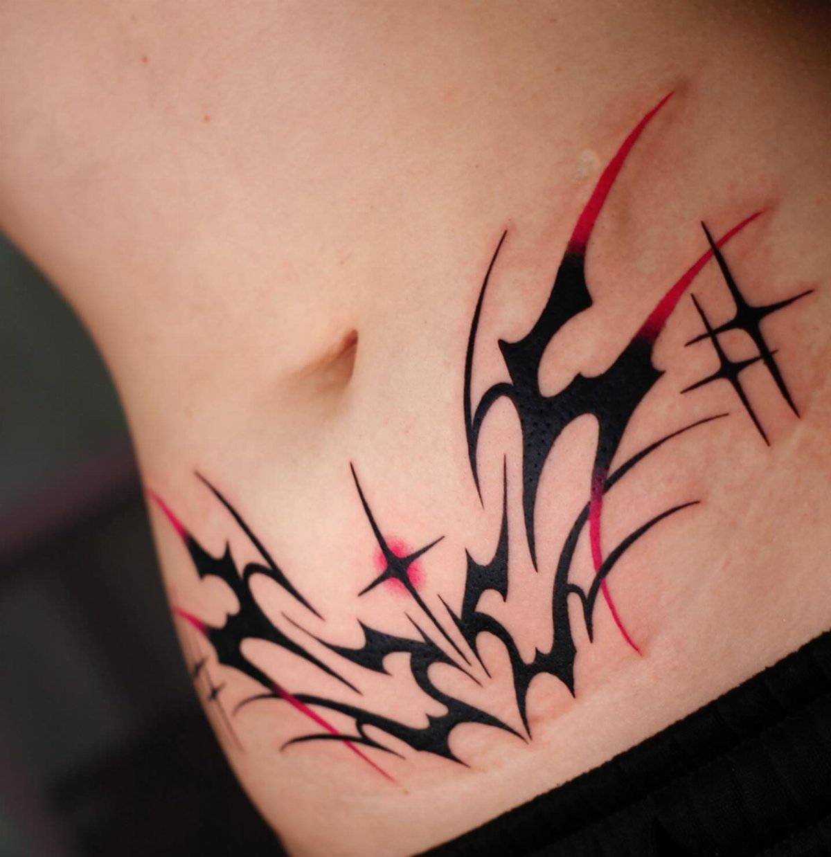 5 Wrap Around Waist Tattoo Ideas That Follow Your Body's Curve 2 A black and red tribal tattoo wrapping around a person's waist and hip.