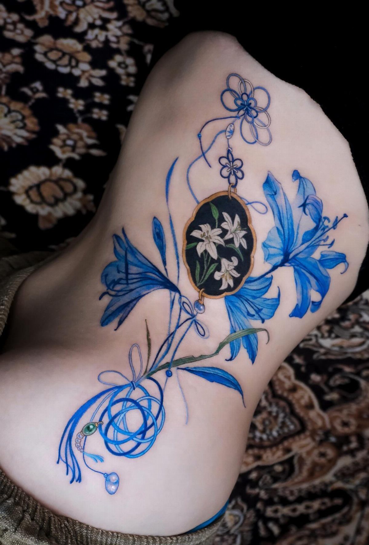 5 Wrap Around Waist Tattoo Ideas That Follow Your Body's Curve 5 A large blue floral tattoo with a central cameo design wraps around a person's waist.