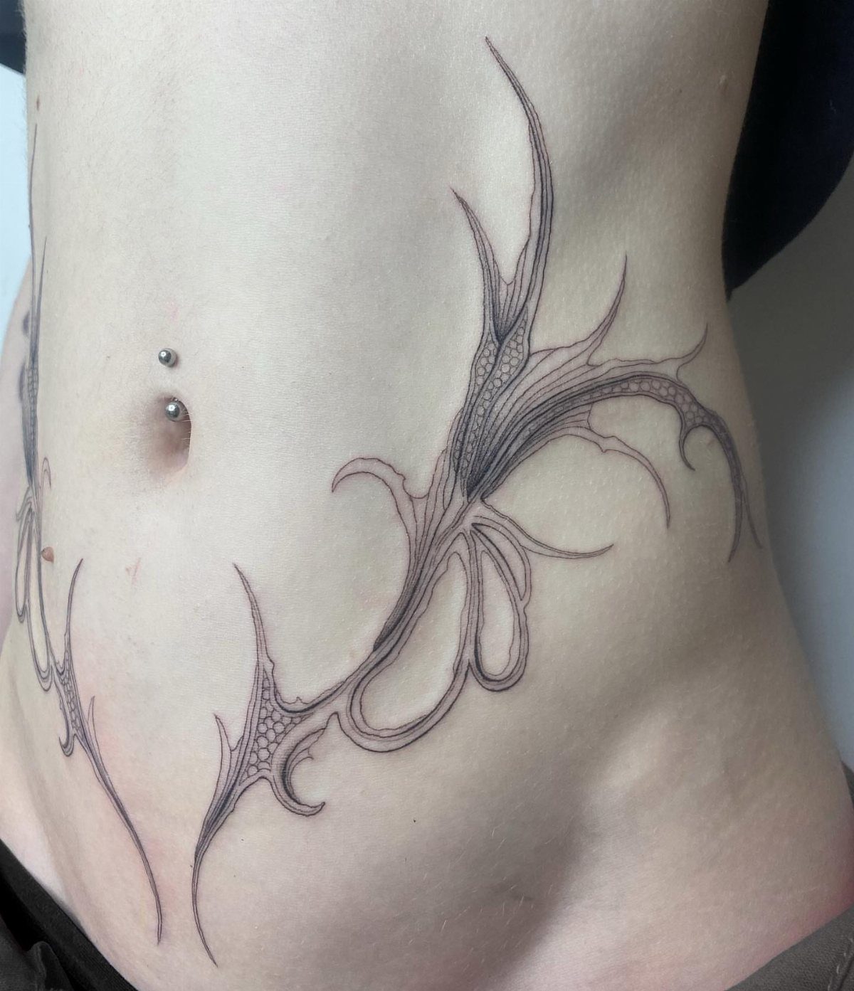 5 Wrap Around Waist Tattoo Ideas That Follow Your Body's Curve 4 A black ink tribal tattoo with flowing organic lines curves around a person's waist and hip.